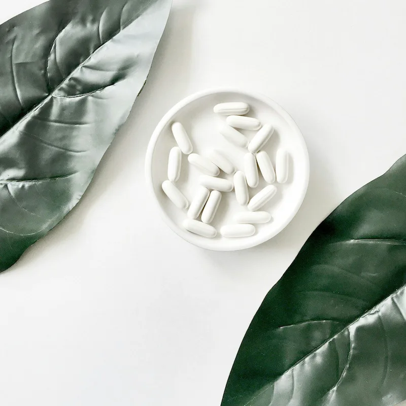 pills in bowl surrounded by large green leafs